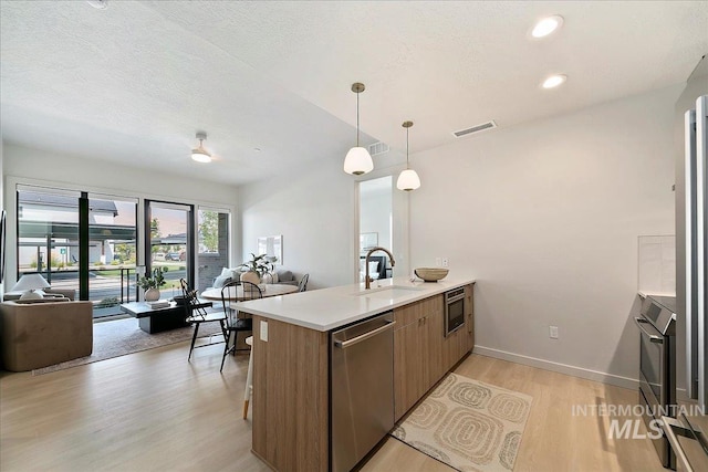 kitchen featuring sink, light hardwood / wood-style flooring, stainless steel dishwasher, kitchen peninsula, and pendant lighting