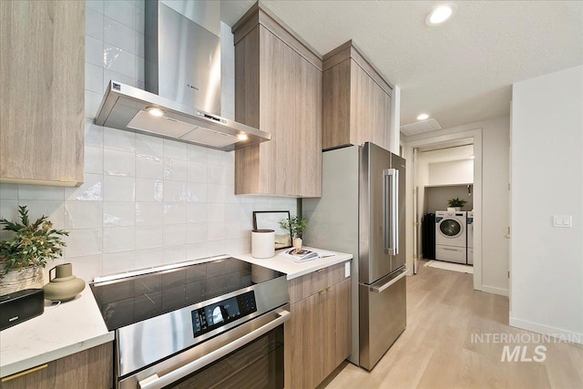 kitchen with wall chimney range hood, washing machine and dryer, tasteful backsplash, light hardwood / wood-style floors, and range