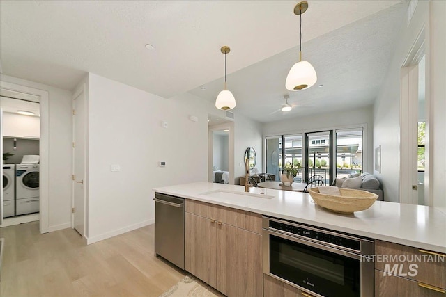 kitchen featuring sink, light hardwood / wood-style flooring, decorative light fixtures, washer and clothes dryer, and appliances with stainless steel finishes