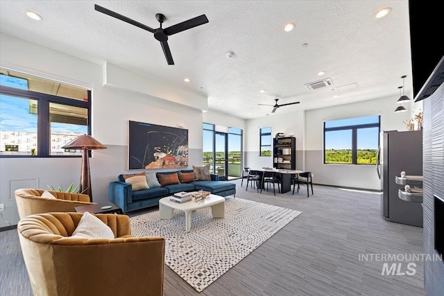 living room with ceiling fan, plenty of natural light, and a textured ceiling