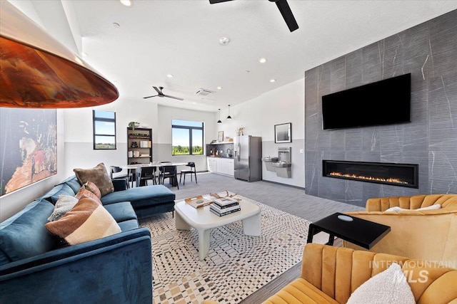 living room featuring ceiling fan and a tiled fireplace