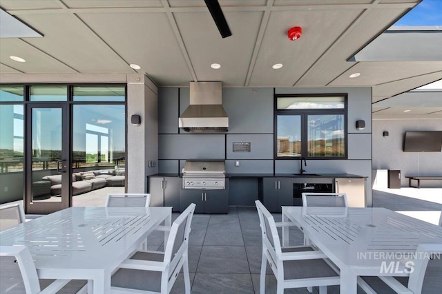 kitchen featuring sink, dark tile patterned flooring, wall chimney range hood, and a wall of windows