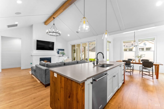 kitchen featuring light wood-style floors, stainless steel dishwasher, a sink, beamed ceiling, and an inviting chandelier