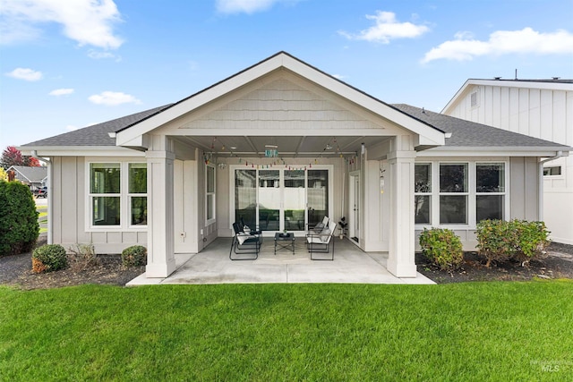 back of house featuring board and batten siding, roof with shingles, a lawn, a patio, and outdoor lounge area