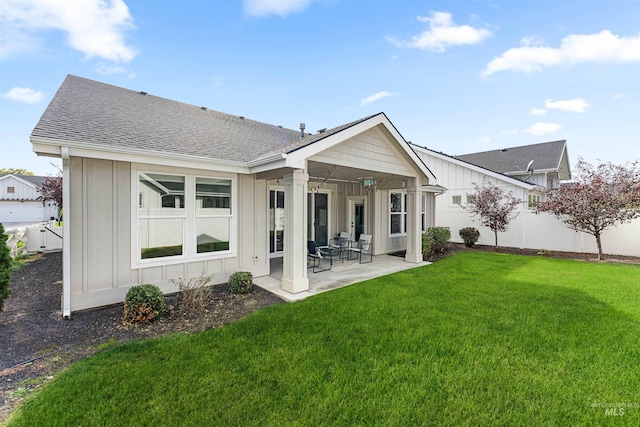 rear view of property featuring roof with shingles, board and batten siding, a fenced backyard, a patio area, and a lawn