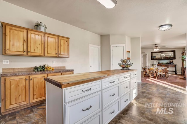 kitchen with ceiling fan, a center island, dark tile patterned floors, and wood counters