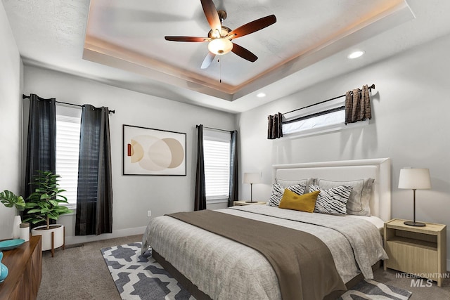 carpeted bedroom featuring a raised ceiling, a ceiling fan, and baseboards