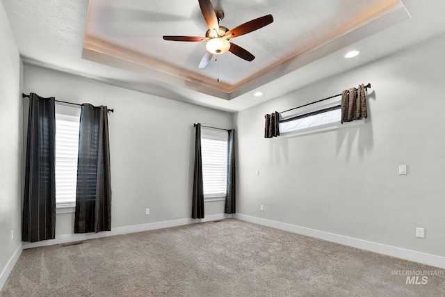 carpeted empty room with a ceiling fan, a tray ceiling, visible vents, and baseboards