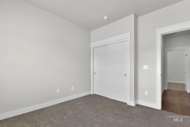 unfurnished bedroom featuring dark colored carpet, a closet, visible vents, and baseboards