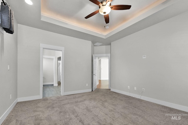 unfurnished bedroom with carpet floors, a tray ceiling, and baseboards