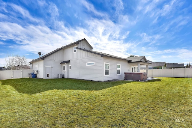 rear view of property featuring a fenced backyard, a yard, and a hot tub