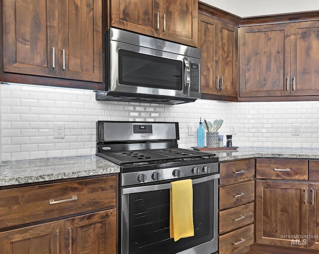 kitchen featuring appliances with stainless steel finishes, backsplash, dark brown cabinetry, and light stone countertops