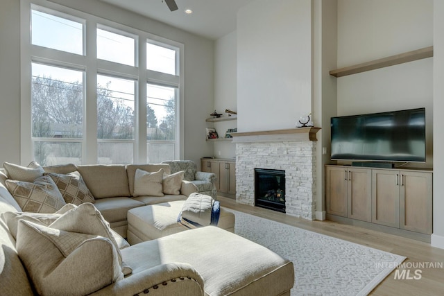 living room with a fireplace, ceiling fan, light hardwood / wood-style flooring, and a towering ceiling