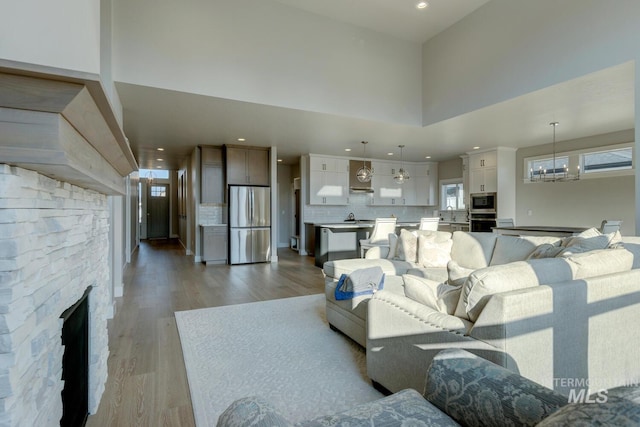 living room featuring a fireplace, a high ceiling, an inviting chandelier, and light hardwood / wood-style flooring