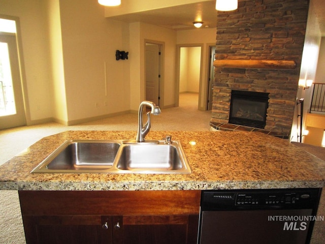 kitchen with a sink, dishwasher, a stone fireplace, carpet flooring, and light stone counters