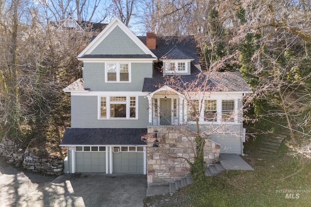 shingle-style home featuring gravel driveway, roof with shingles, a chimney, and an attached garage