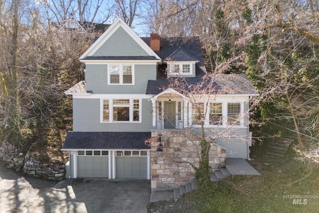 shingle-style home featuring gravel driveway, roof with shingles, a chimney, and an attached garage