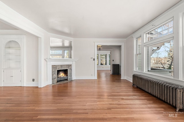 unfurnished living room with built in features, light wood-style flooring, and radiator heating unit