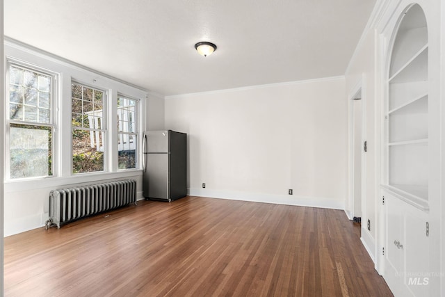 empty room with ornamental molding, radiator, dark wood finished floors, and built in shelves