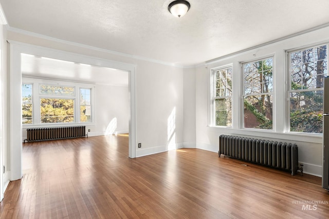 empty room featuring radiator heating unit, a textured ceiling, crown molding, and wood finished floors