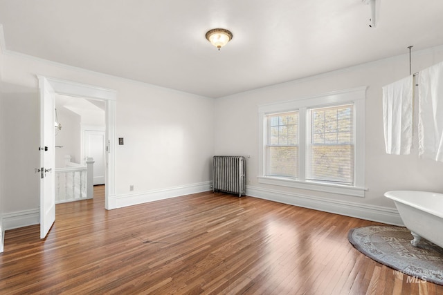 spare room featuring radiator, wood-type flooring, baseboards, and crown molding