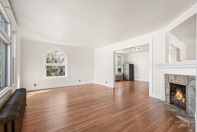 unfurnished living room with radiator heating unit, a fireplace, baseboards, and wood finished floors