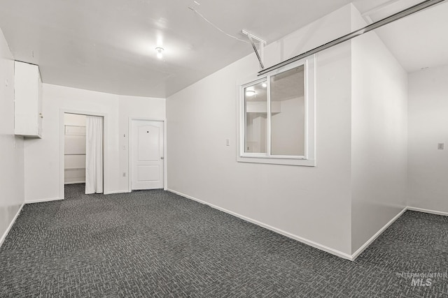 empty room featuring dark colored carpet and baseboards