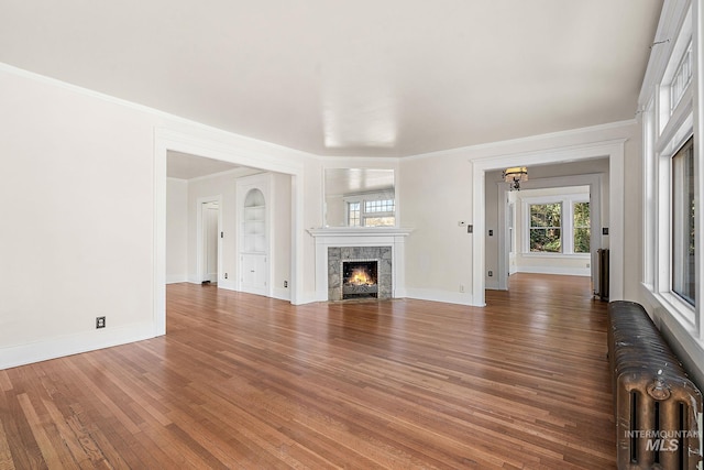 unfurnished living room featuring baseboards, radiator heating unit, a premium fireplace, ornamental molding, and wood finished floors