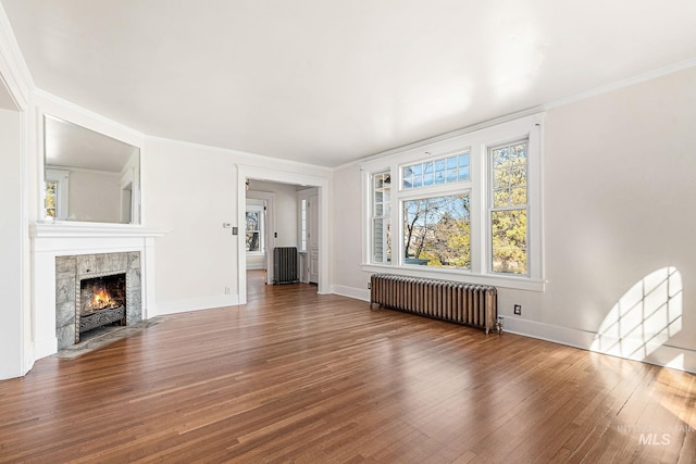 unfurnished living room featuring crown molding, a fireplace, radiator, wood finished floors, and baseboards