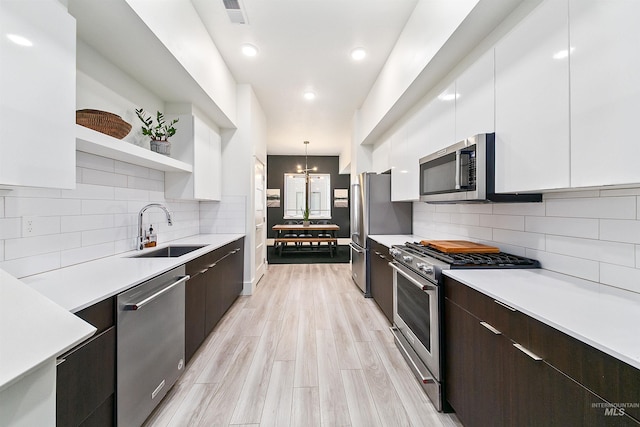 kitchen featuring stainless steel appliances, sink, white cabinets, dark brown cabinets, and pendant lighting