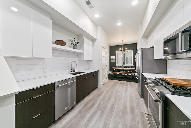 kitchen featuring stainless steel appliances, sink, white cabinets, hanging light fixtures, and a chandelier