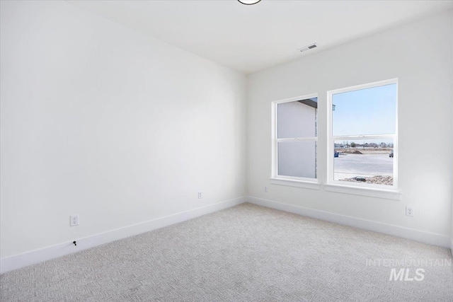 spare room featuring light carpet, visible vents, and baseboards