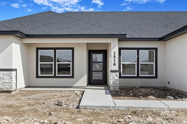 view of exterior entry with a shingled roof and stucco siding