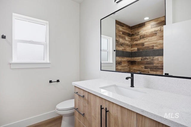 bathroom with toilet, plenty of natural light, baseboards, and vanity