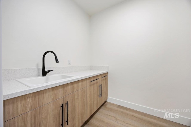 laundry room featuring light wood-style floors, a sink, and baseboards