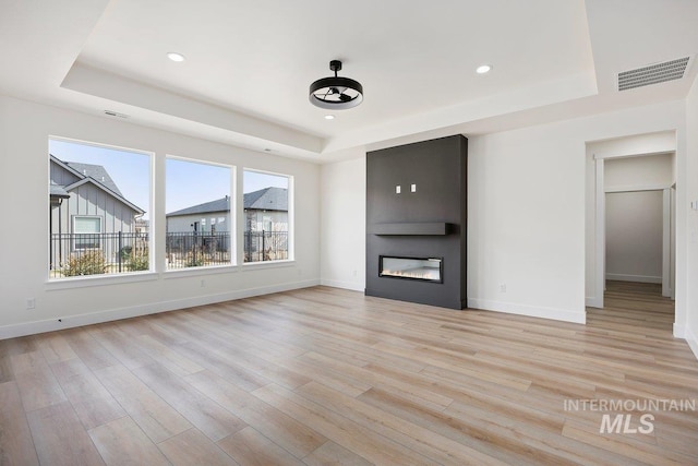 unfurnished living room featuring a large fireplace, visible vents, and a raised ceiling