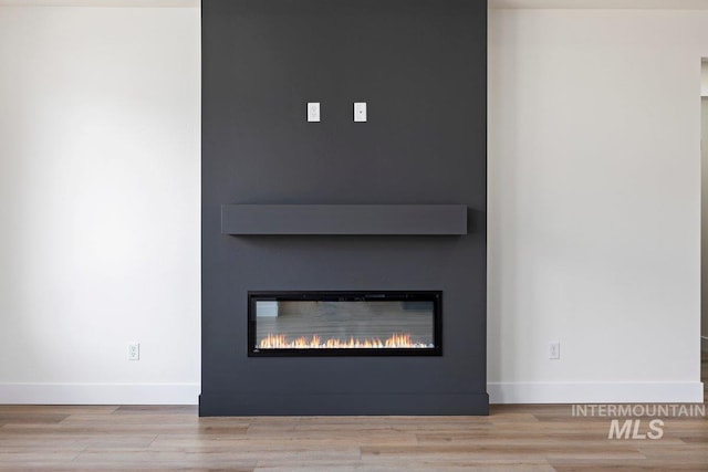 room details featuring a large fireplace, baseboards, and wood finished floors