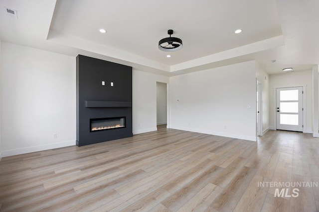 unfurnished living room with a tray ceiling, a fireplace, visible vents, light wood-style floors, and baseboards