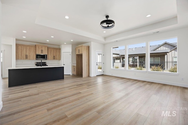 kitchen featuring baseboards, stainless steel microwave, a tray ceiling, light countertops, and light wood-style floors