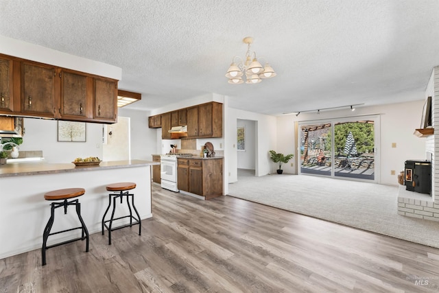 kitchen with light wood-type flooring, white range with gas stovetop, under cabinet range hood, open floor plan, and a chandelier