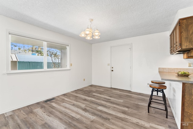 unfurnished dining area with a textured ceiling, an inviting chandelier, visible vents, and light wood-type flooring