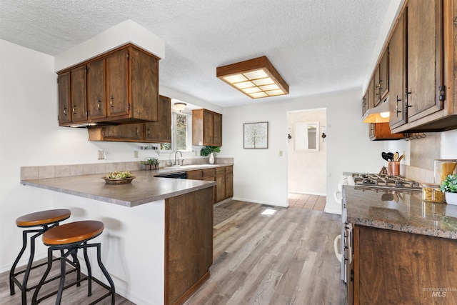 kitchen with a peninsula, a sink, a textured ceiling, a kitchen breakfast bar, and light wood-type flooring