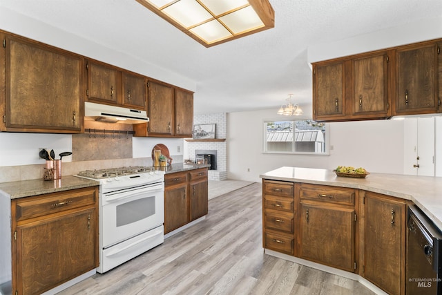 kitchen with light wood-style flooring, white gas range oven, under cabinet range hood, dishwasher, and a brick fireplace