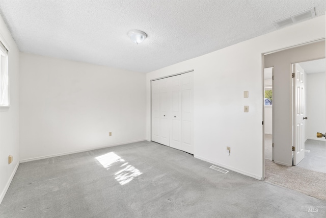 unfurnished bedroom with visible vents, carpet floors, a textured ceiling, and a closet