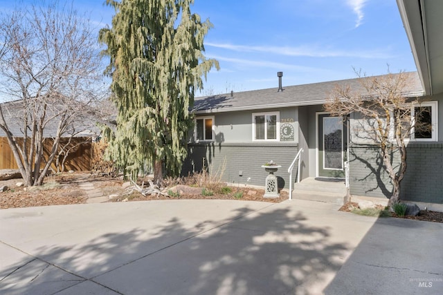 view of front of home featuring a patio, brick siding, and fence