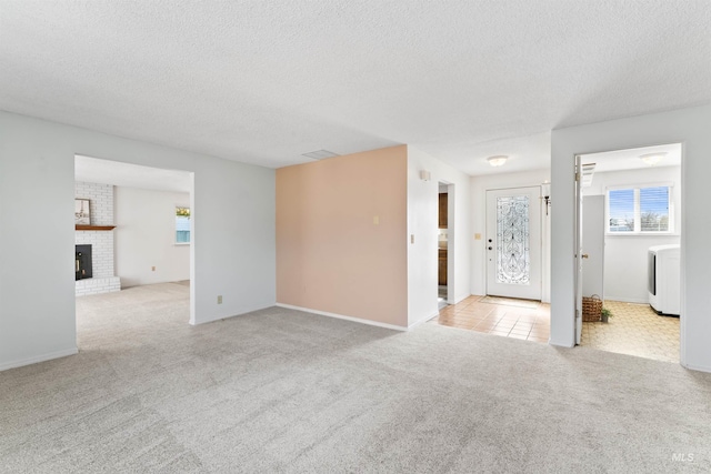 unfurnished living room with carpet flooring, washer / dryer, a brick fireplace, and a textured ceiling