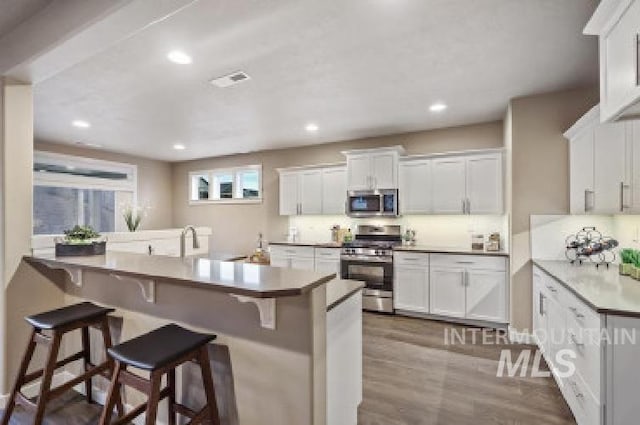 kitchen with hardwood / wood-style flooring, white cabinetry, appliances with stainless steel finishes, and a kitchen bar