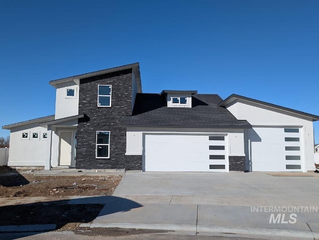 modern home with a garage, stone siding, driveway, and stucco siding