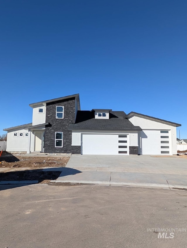 view of front of property with driveway, stone siding, an attached garage, and stucco siding