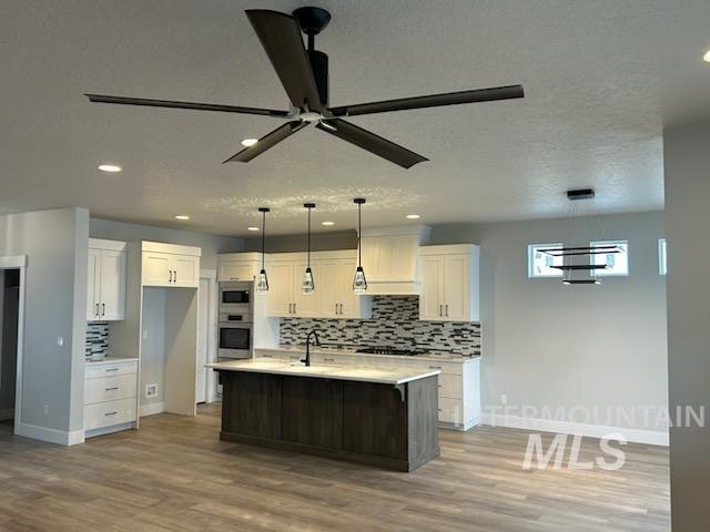 kitchen featuring stainless steel appliances, light countertops, backsplash, white cabinetry, and ceiling fan